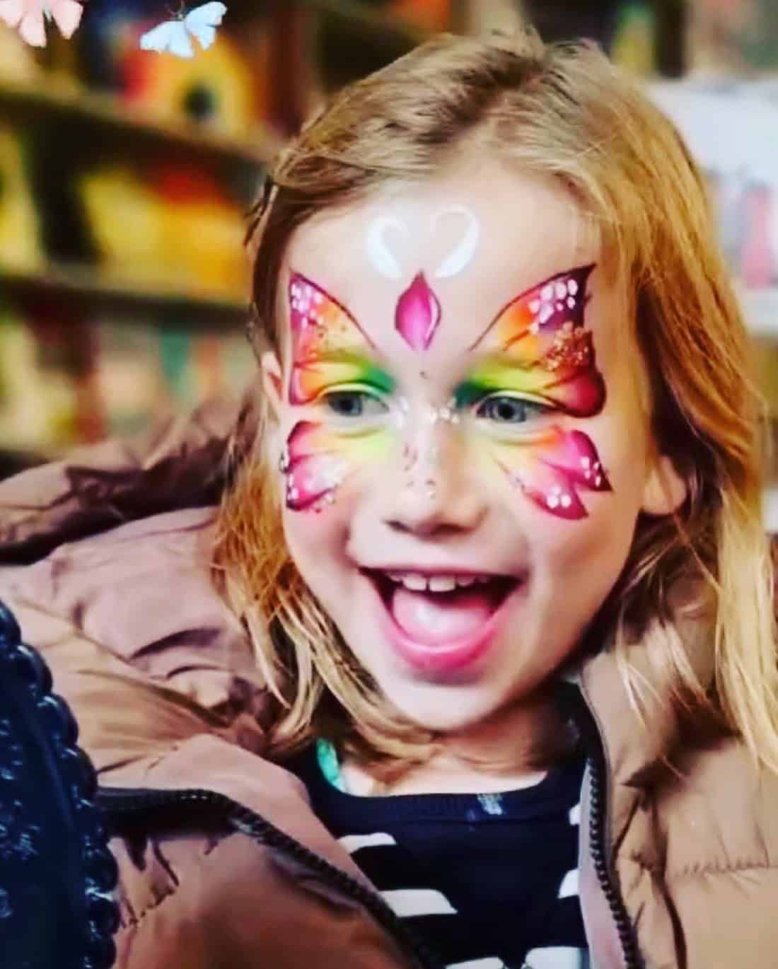 Lachend meisje met een regenboogvlinder over haar hele gezicht