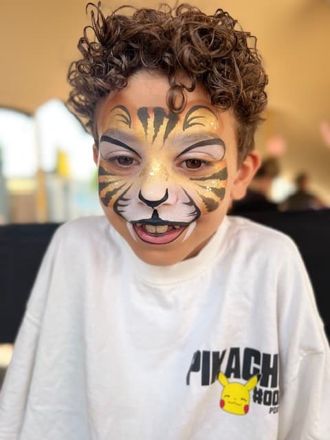 Jongen met een gouden tijger met zwarte strepen en glitter op zijn voorhoofd