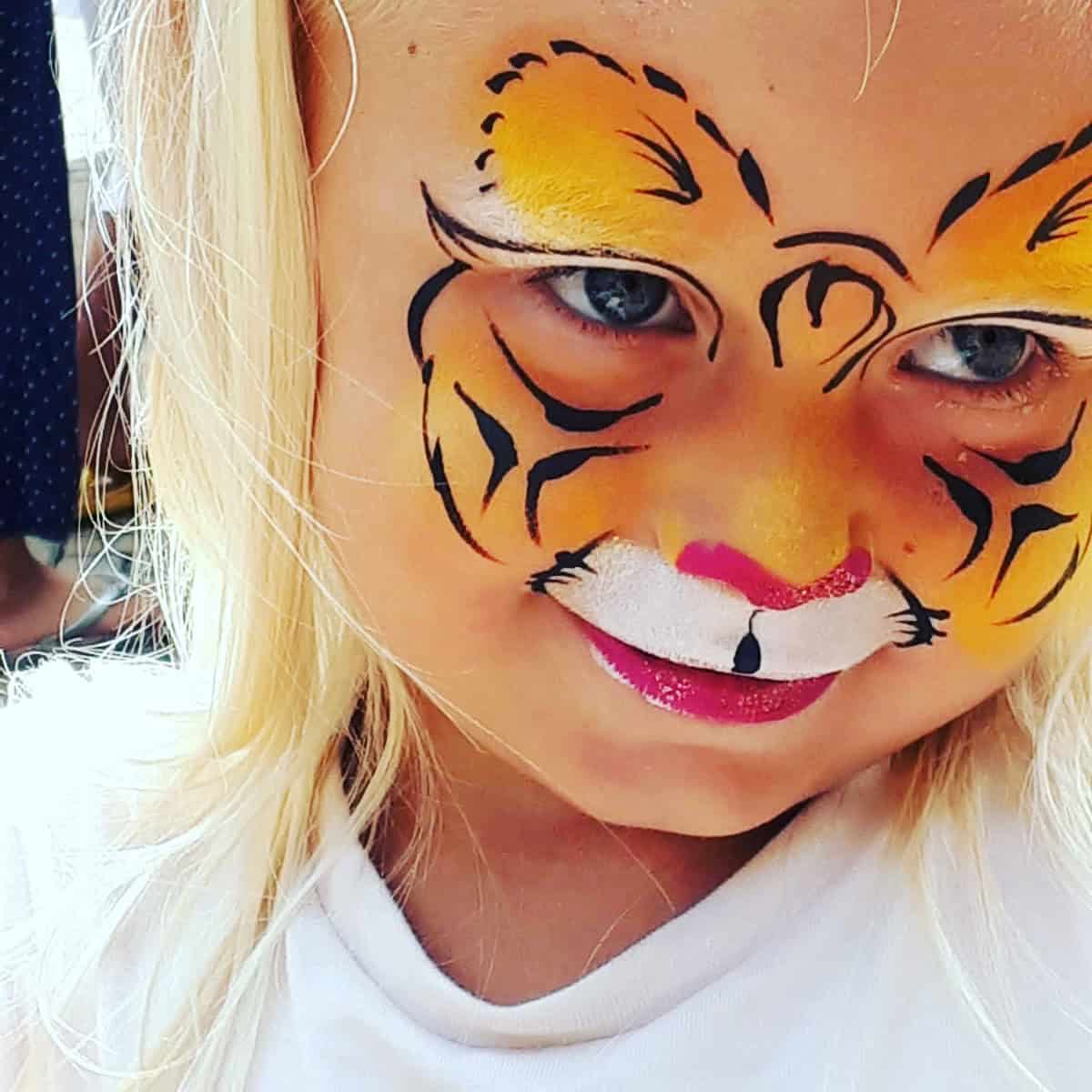Meisje met een geel met oranje tijger over haar hele gezicht en roze lippen