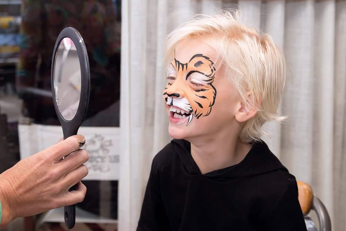 Jongen bekijkt zijn oranje tijgerschmink lachend in de spiegel