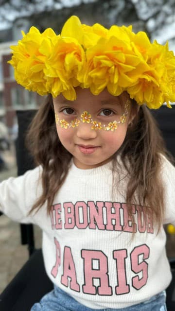 Meisje met een gele bloemenkrans en kleine gele bloemetjes met glitter onder haar ogen