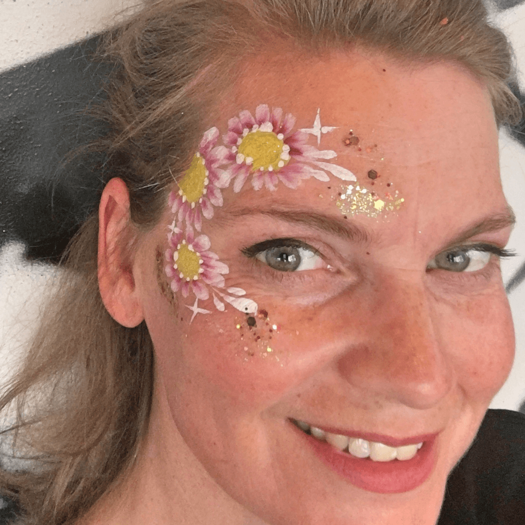 Vrouw met drie roze madeliefjes rond haar oog, afgewerkt met gouden glitter