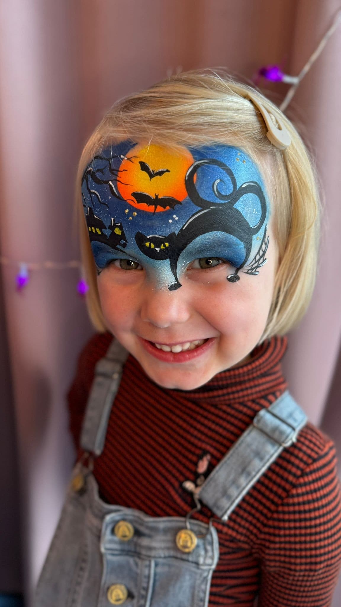 Meisje met een halloweentafereel op haar voorhoofd: oranje maan, vleermuizen en zwarte katten