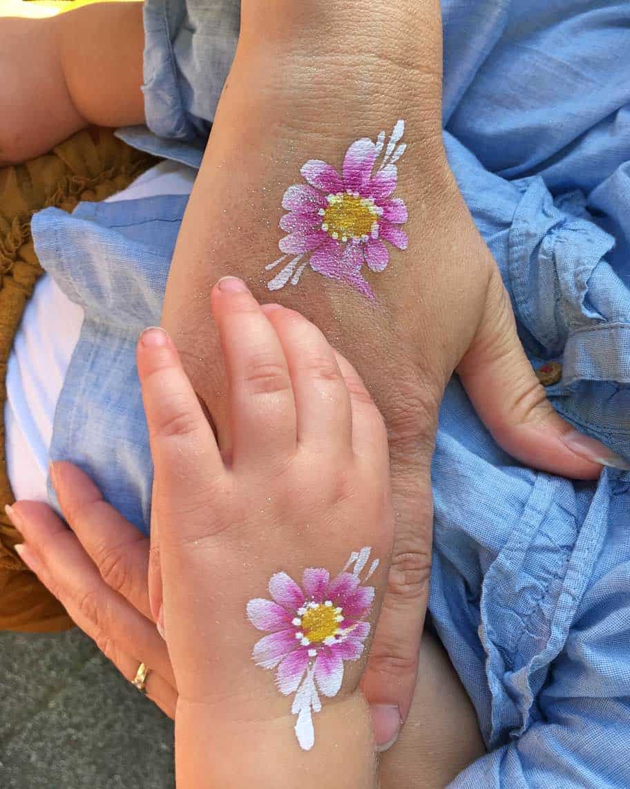 Grote en kleine hand naast elkaar, allebei met een roze bloem op de rug geschilderd
