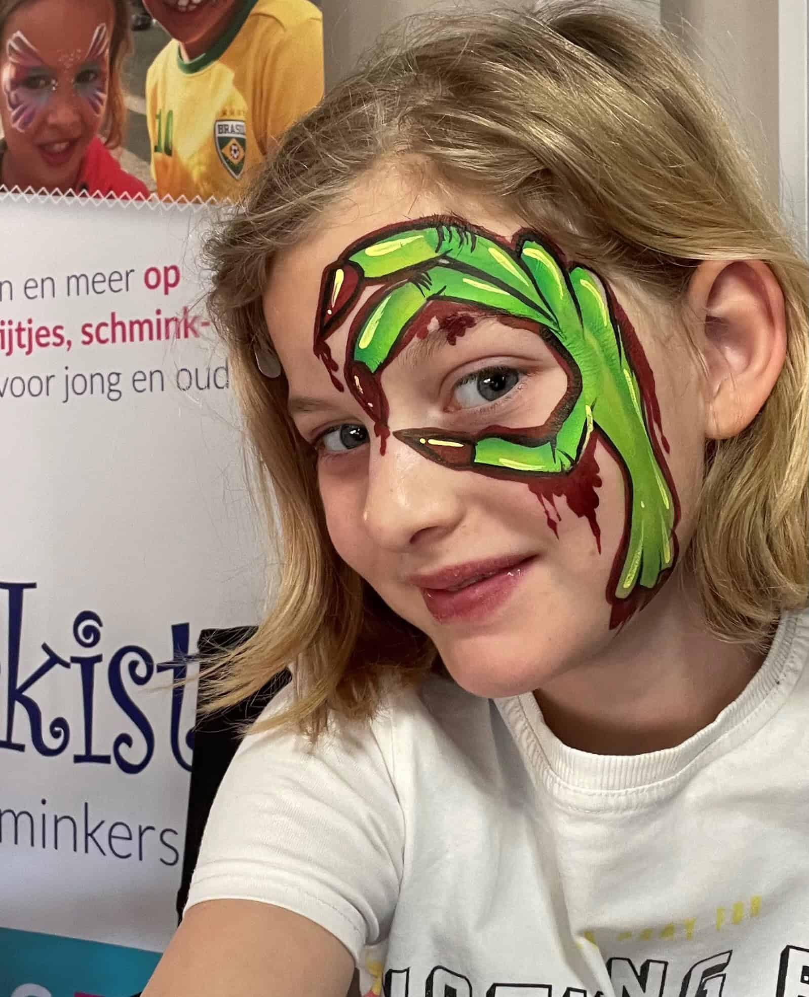Meisje met een groene zombiehand en bloedstrepen over haar oog geschminkt