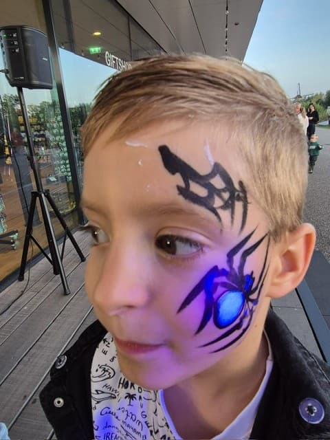 Jongen met een zwart spinnenweb op zijn voorhoofd en een spin met blauwe rug op zijn wang