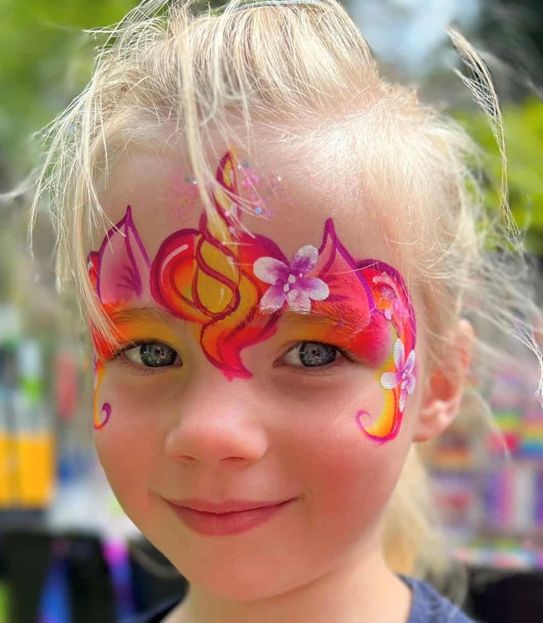 Meisje met een vuurrode eenhoorn met gele hoorn en paarse bloemen rond haar ogen