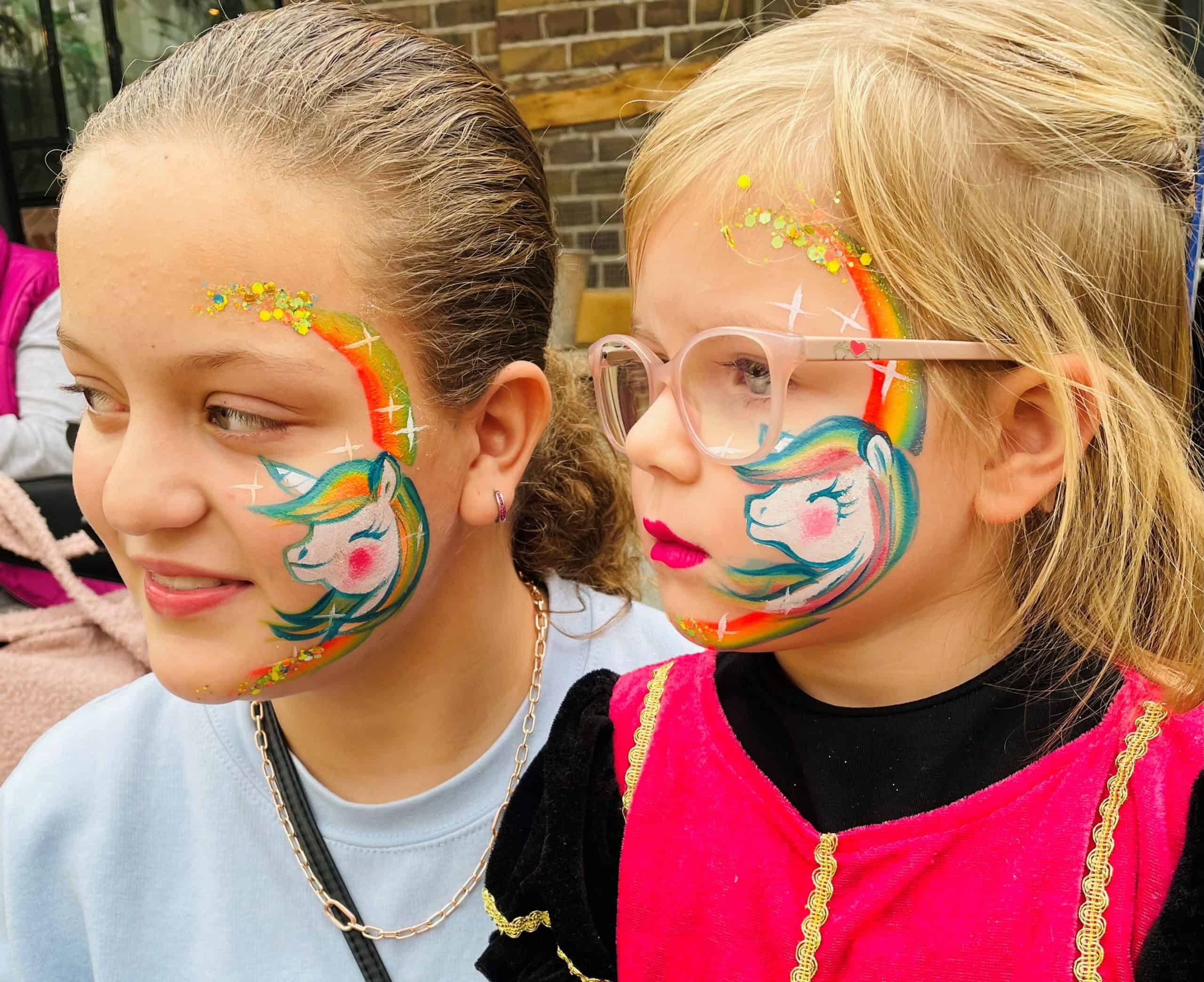 Twee meisjes met een eenhoorn met regenboogmanen op hun wang