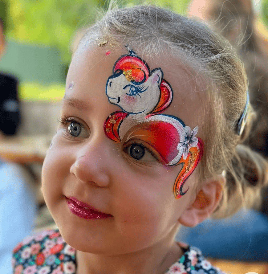 Meisje met een getekend eenhoornhoofdje met oranje manen naast haar oog